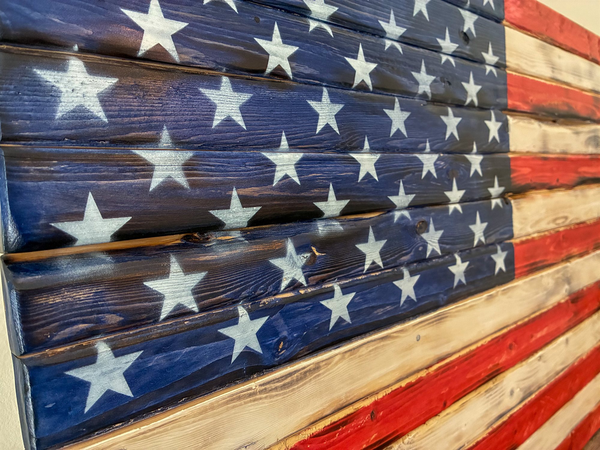 Close-up of a handcrafted wood American flag's torch-burned star field — white stenciled stars on charred navy pine flowing into red and cream stripes, solid wood made by hand in Trussville, Alabama