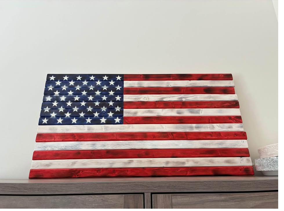Handcrafted rustic wood American flag with hand-stained red and white pine stripes and stenciled spray-painted white stars, displayed on a console table