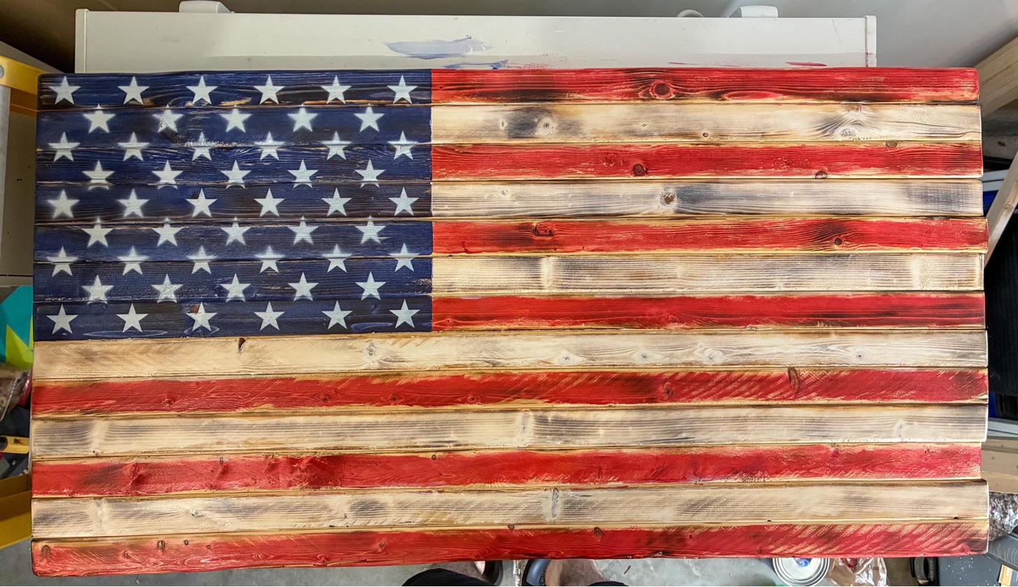 Rustic torch-burned wood American flag with hand-stained stripes and spray-painted stars on a stained blue field, made in Alabama