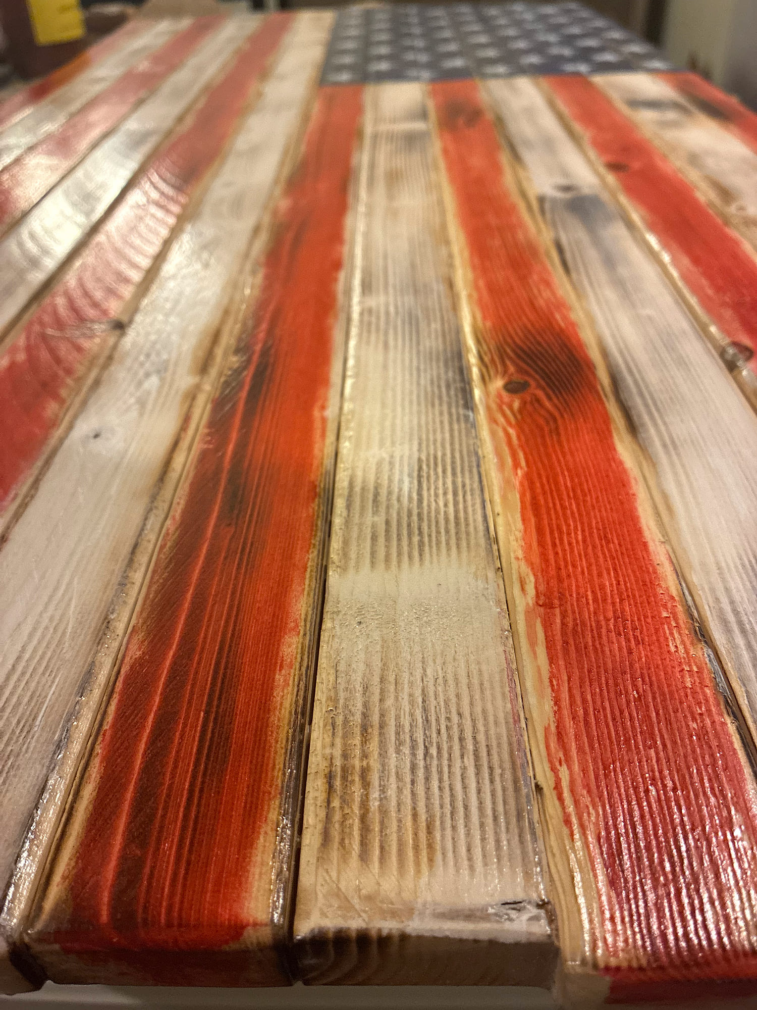 Angled view down the distressed, hand-stained pine stripes of a rustic wood American flag toward the stenciled star field