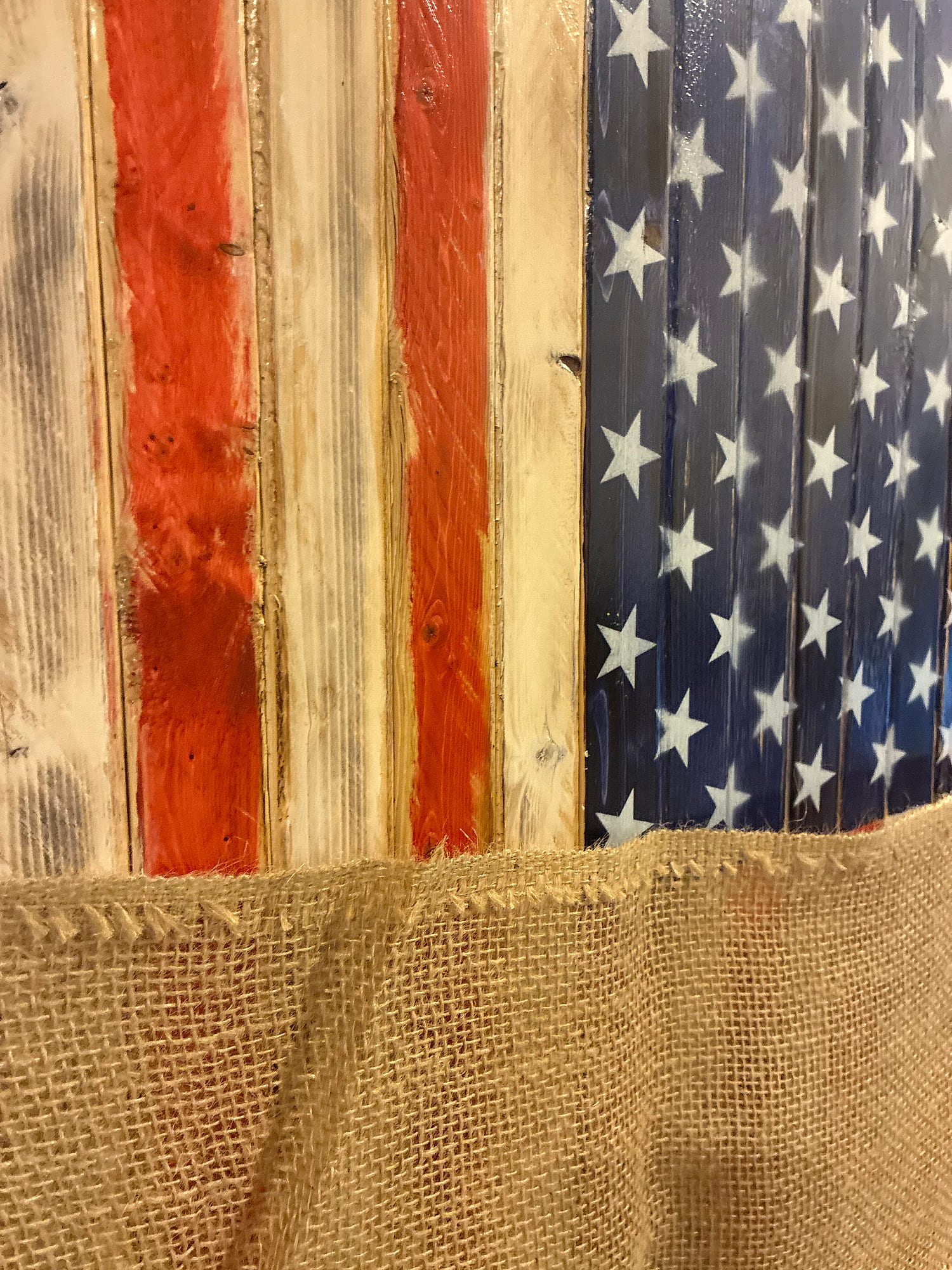 Handcrafted rustic wood American flag with hand-stained red and white stripes and stenciled white stars, resting on natural burlap before wrapping in the Trussville, Alabama shop