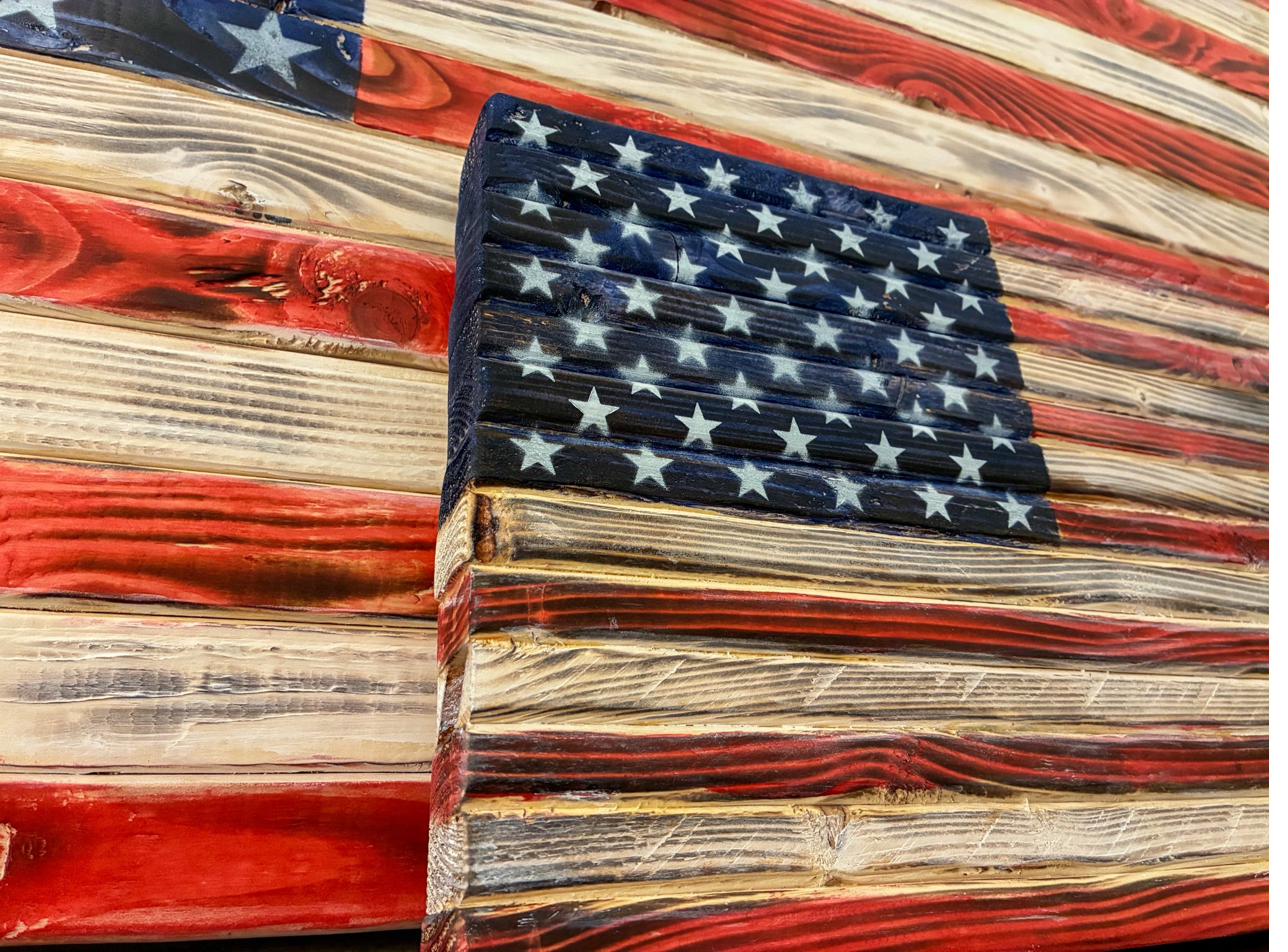 Close-up of the stenciled, spray-painted white stars and deep blue field of a rustic wood American flag, showing the charred pine grain